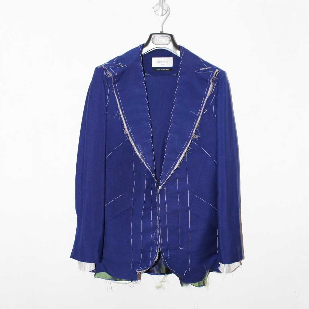 A blue basted jacket with white tacking stitches hanging in front of the pattern rail