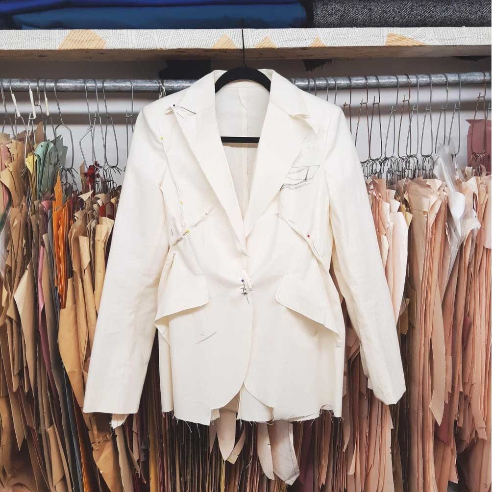 A pinned calico toile jacket hanging among paper patterns in the Orhan workroom