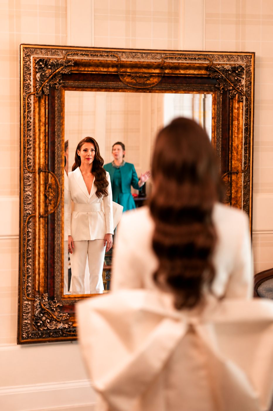 A bride in a white trouser suit seeing herself in the mirror