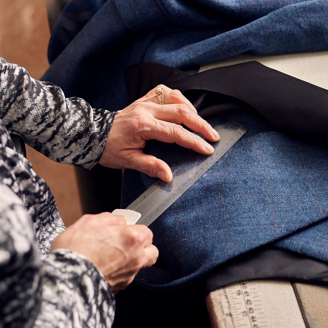 Hands marking a line with a ruler on blue herringbone tweed
