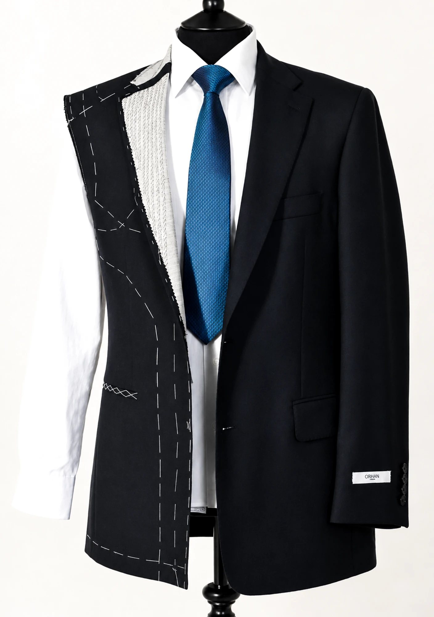 A bespoke jacket shown half finished: basted canvas and chalk lines on one side, the completed suit on the other