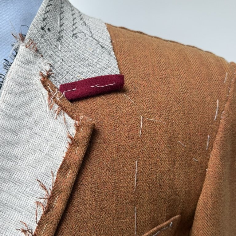 A basted tweed jacket in progress, its canvas and chalk markings still visible at the lapel