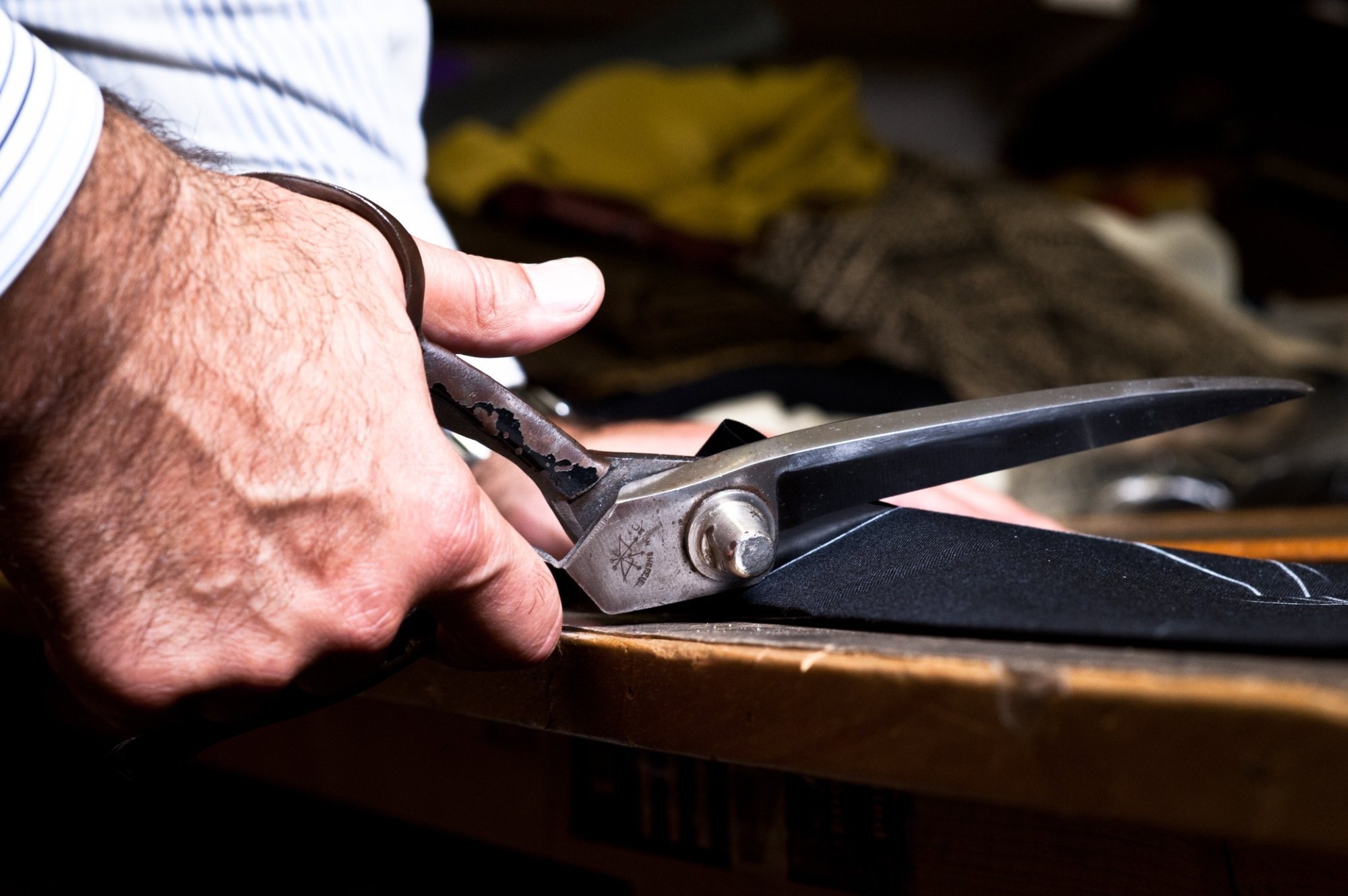 Tailor's shears cutting into navy pinstripe cloth at the bench