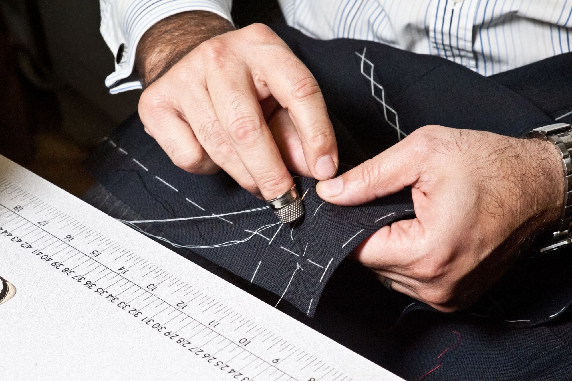 Hand stitching with a thimble through chalk-marked navy cloth