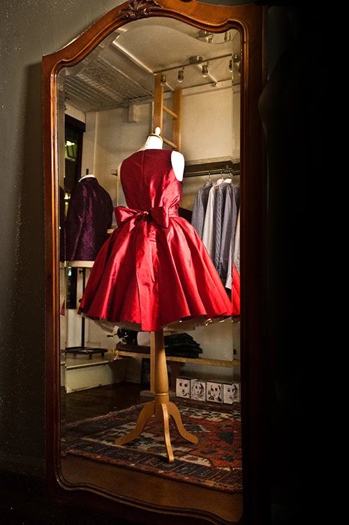 A red taffeta dress on a stand, reflected in the studio mirror among finished jackets