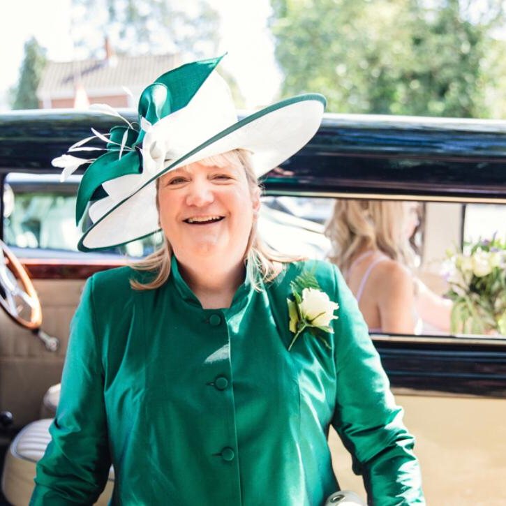 A mother of the bride in an emerald silk coat and occasion hat arriving by vintage car