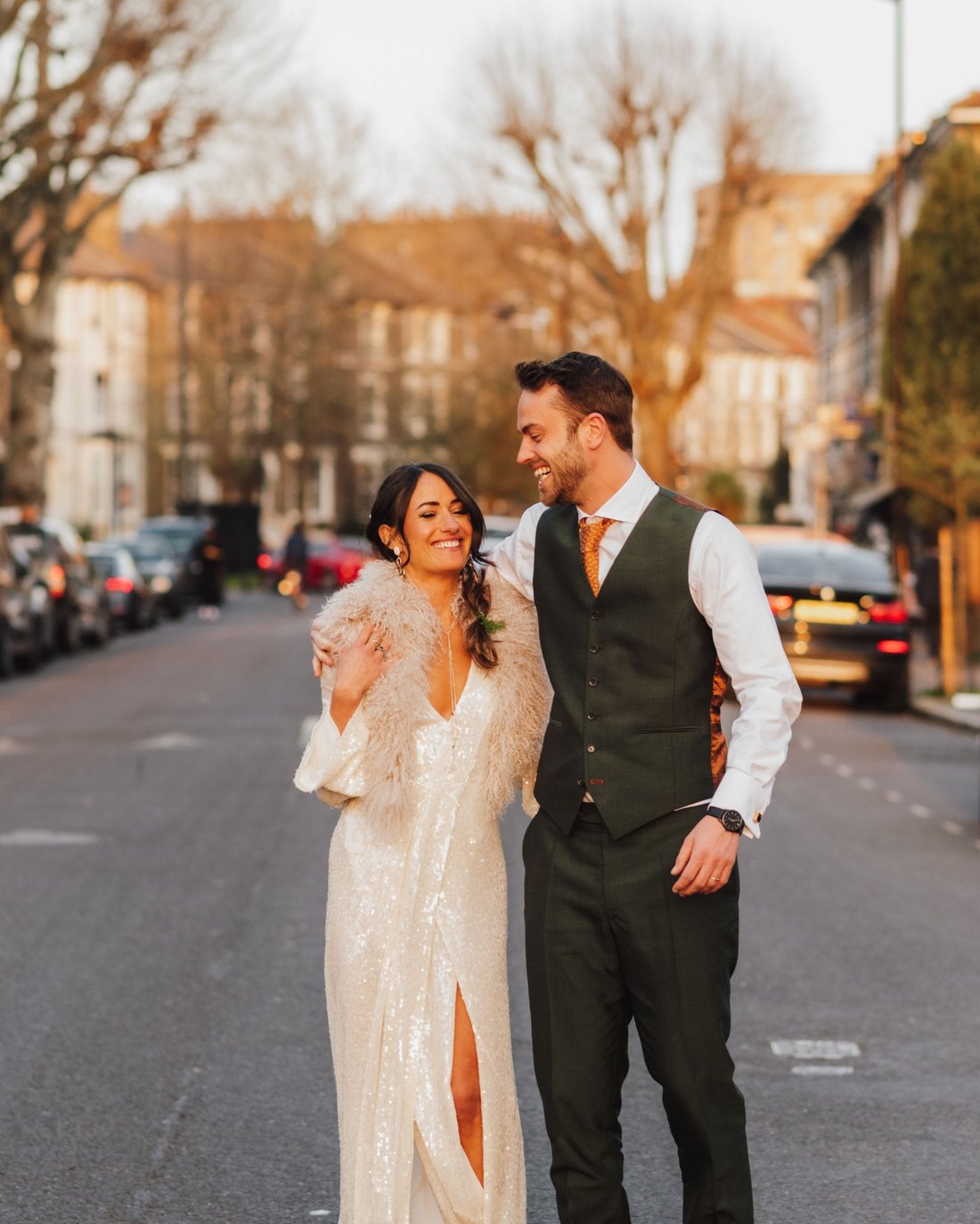 A couple laughing in the road at golden hour, his green waistcoat and trousers perfectly fitted