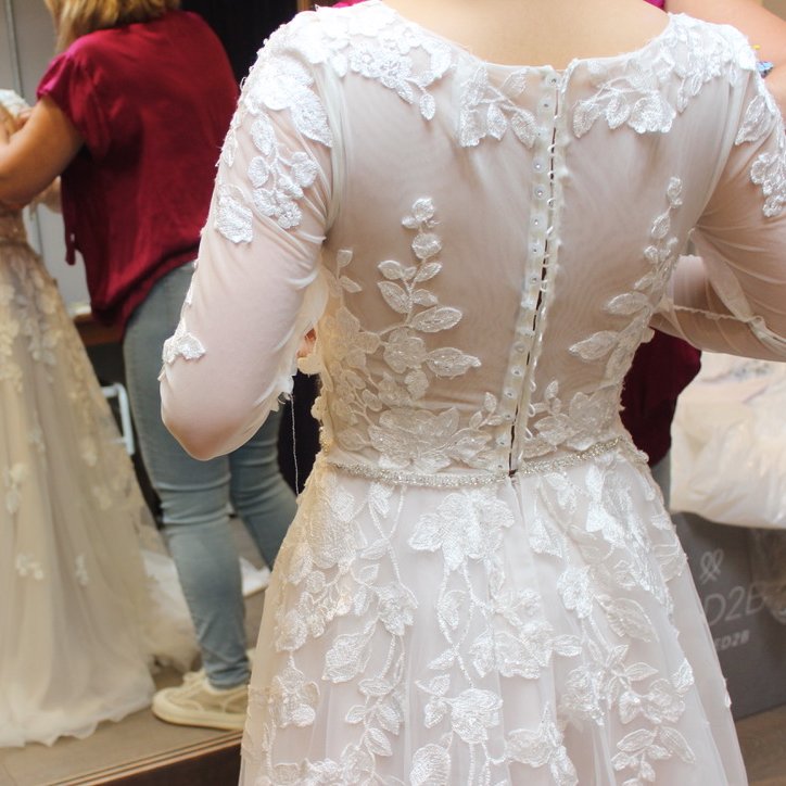 The lace back and button row of a wedding dress during a fitting, the front reflected in the mirror