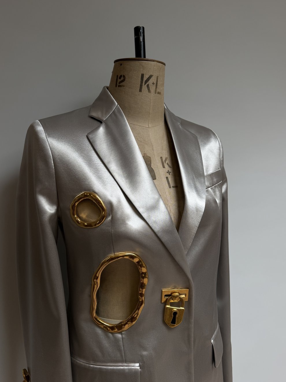 Three-quarter view of the silver satin jacket with gold cut-out frames on the studio stand