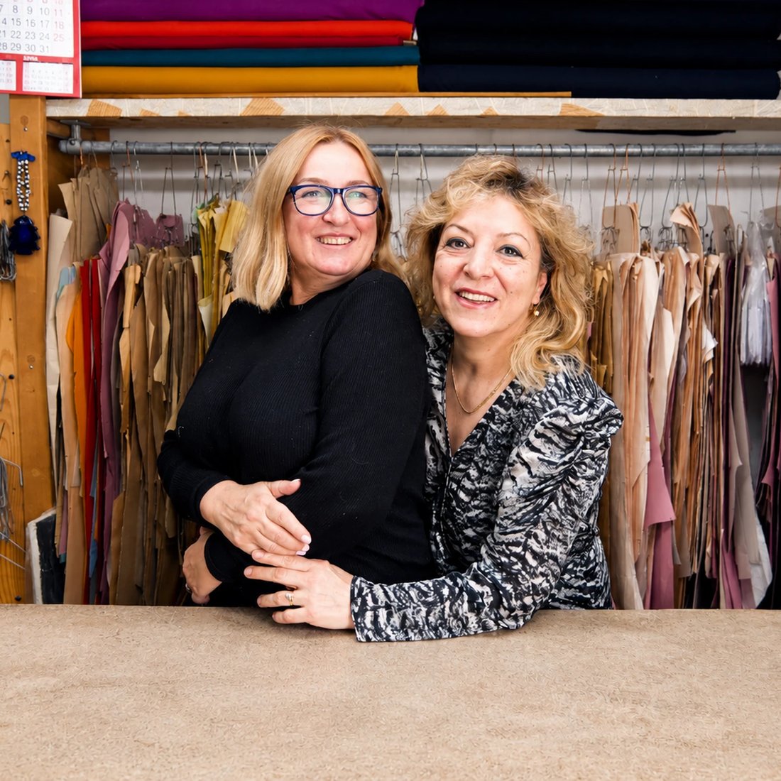 Two of the Orhan team smiling at the cutting bench, paper patterns hanging behind