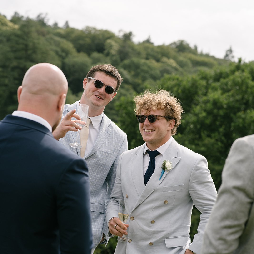 A groom's party in complementary summer suits sharing champagne on the lawn