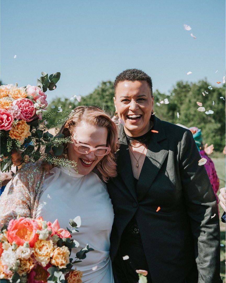 A couple laughing in confetti — a sequinned jacket and white dress beside a black suit