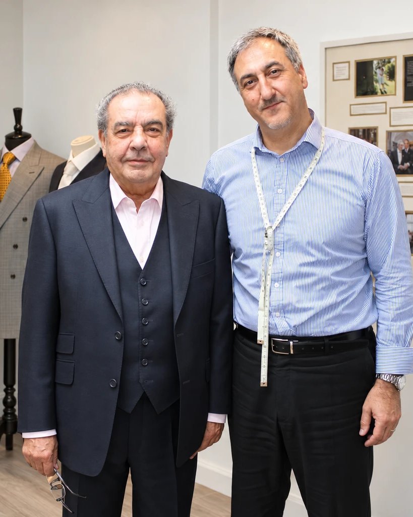 Orhan with a longstanding client in the studio, tape measure around his neck, the wedding board behind them