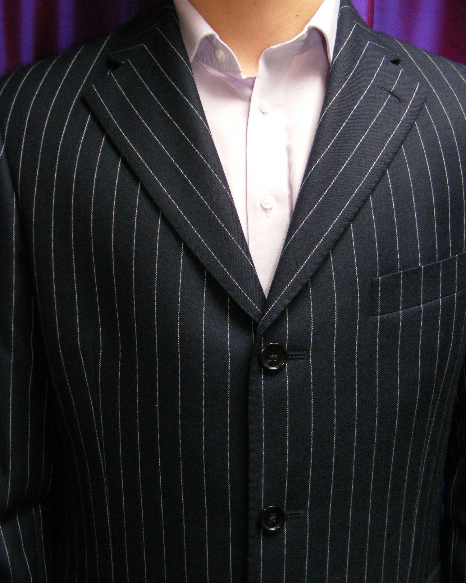 A pale shirt worn open-collared under a navy pinstripe suit