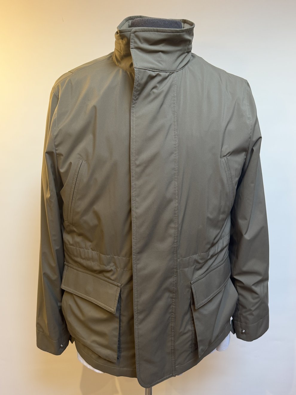 A stone field jacket with a funnel collar and flap pockets on the studio mannequin