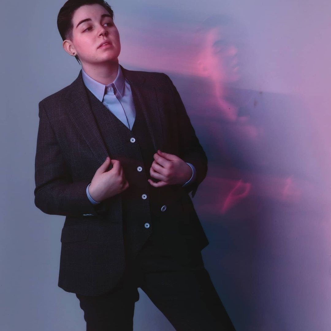A client in a charcoal check three-piece suit, lit in pink and violet studio light