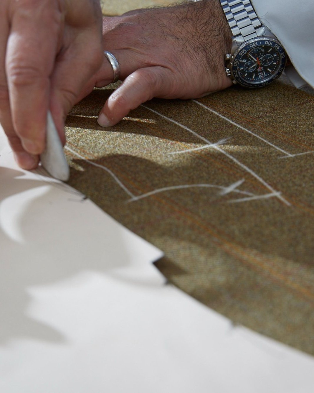 Orhan chalk-marking tweed cloth around a paper pattern, shears at his side