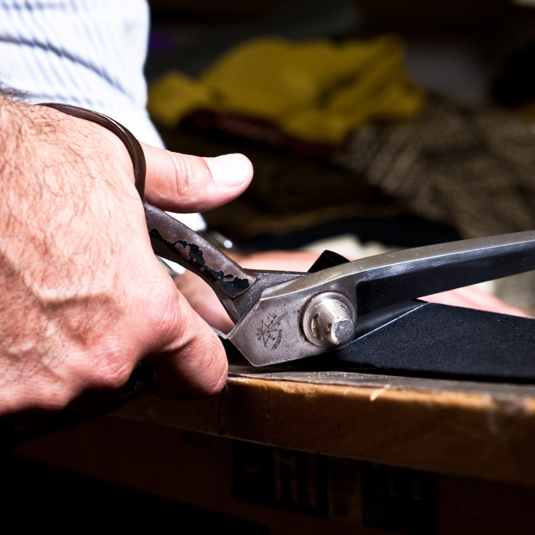 Well-worn tailor's shears cutting into pinstripe cloth at the bench