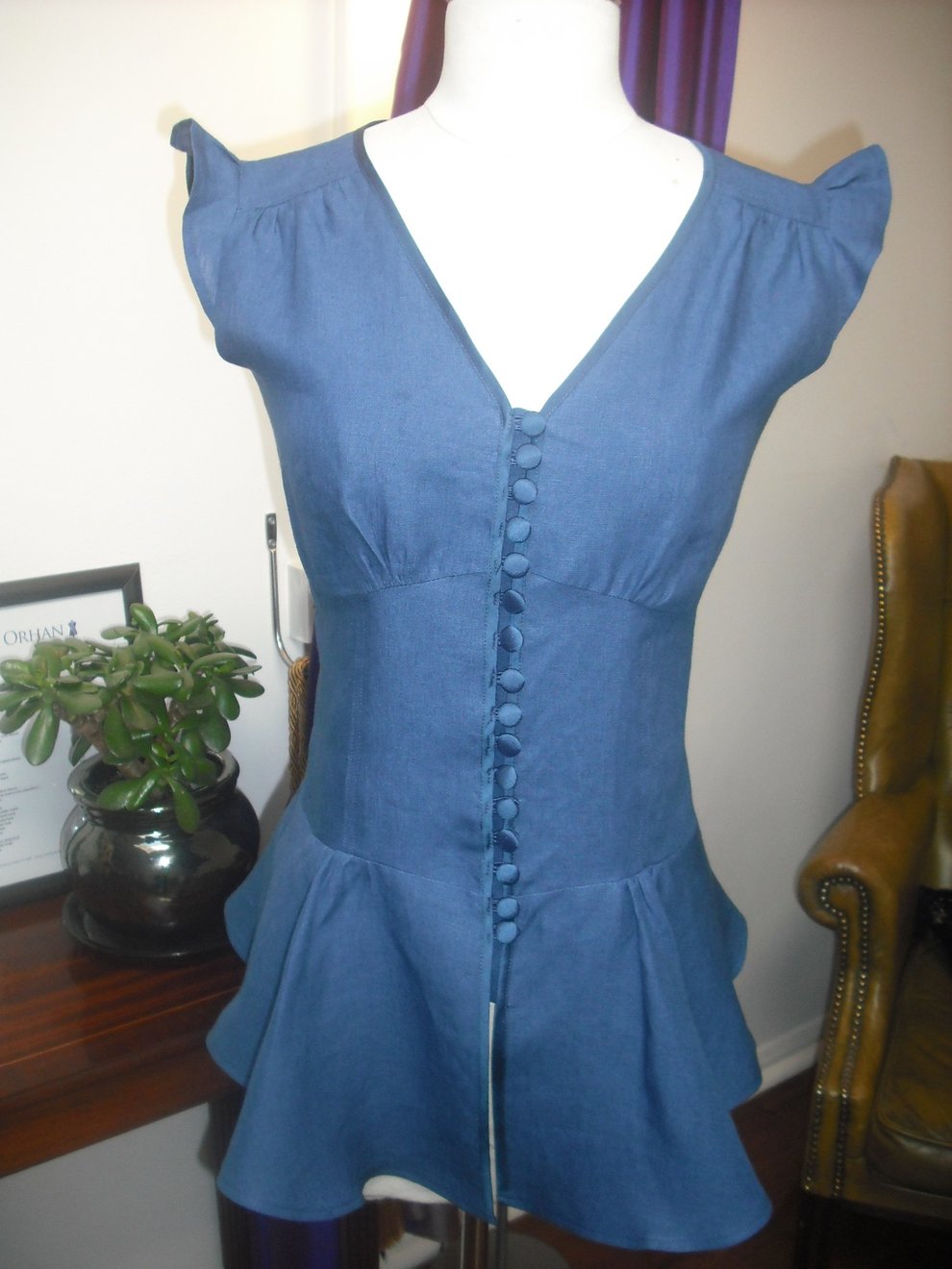 A blue linen blouse with satin buttons, flutter sleeves and a peplum hem