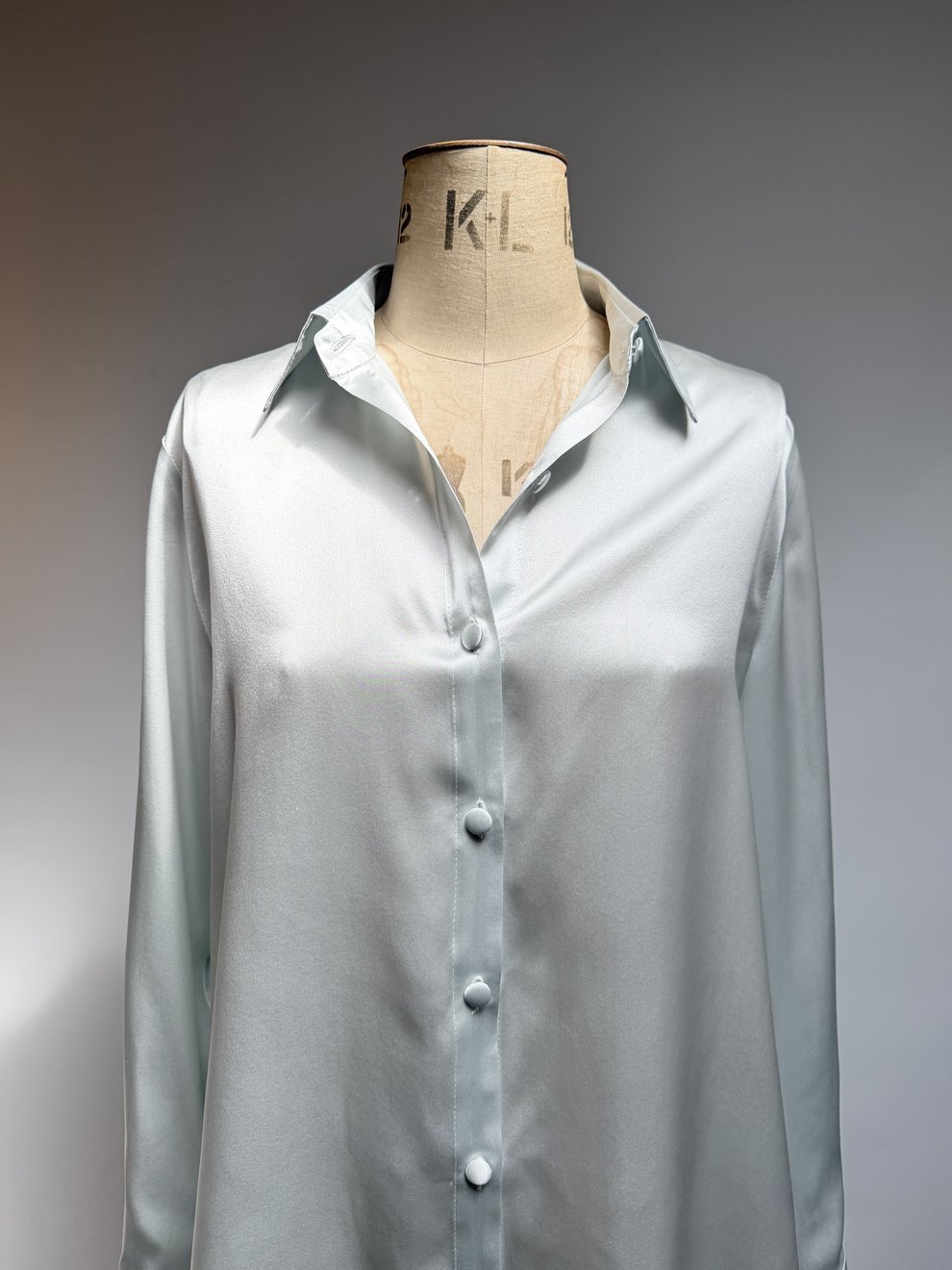 A silver-grey satin shirt buttoned on the tailor's stand