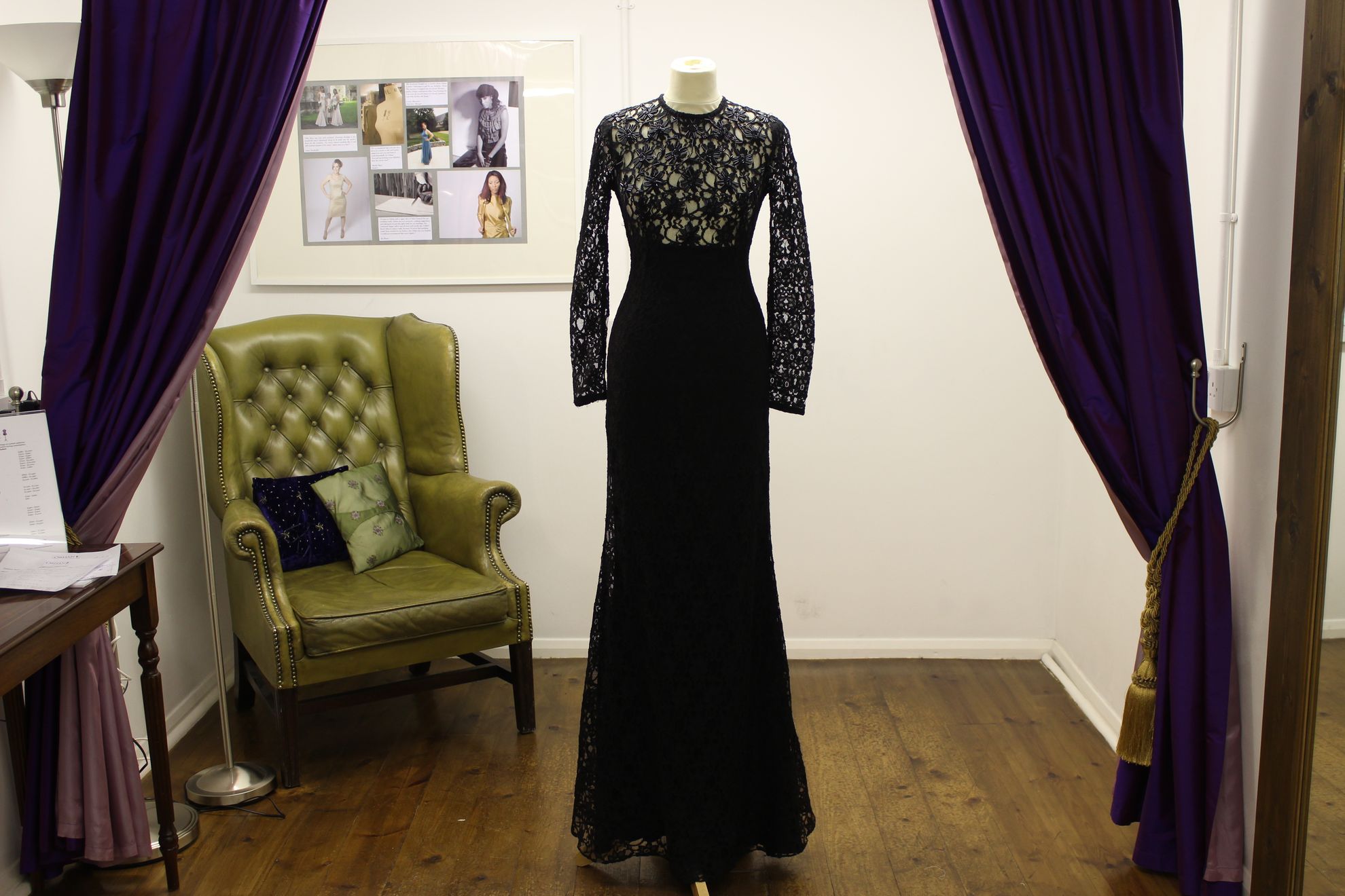 A black lace evening gown in the fitting room between purple curtains